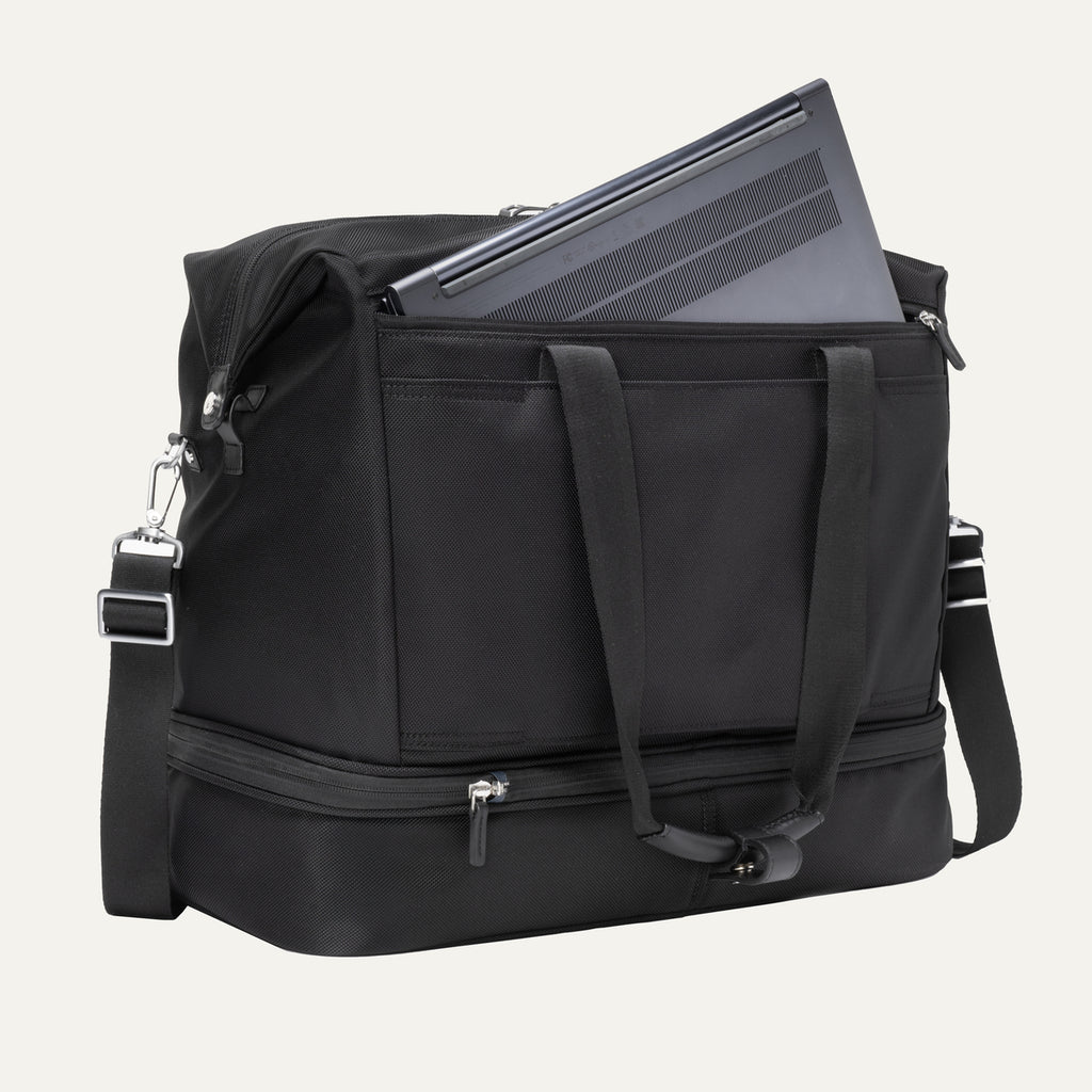 a black travelpro platinum elite drop-bottom weekender bag shown with a grey laptop being inserted into the internal padded electronics sleeve, highlighting the bag's organization and tech protection.