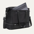 a black travelpro platinum elite drop-bottom weekender bag shown with a grey laptop being inserted into the internal padded electronics sleeve, highlighting the bag's organization and tech protection.