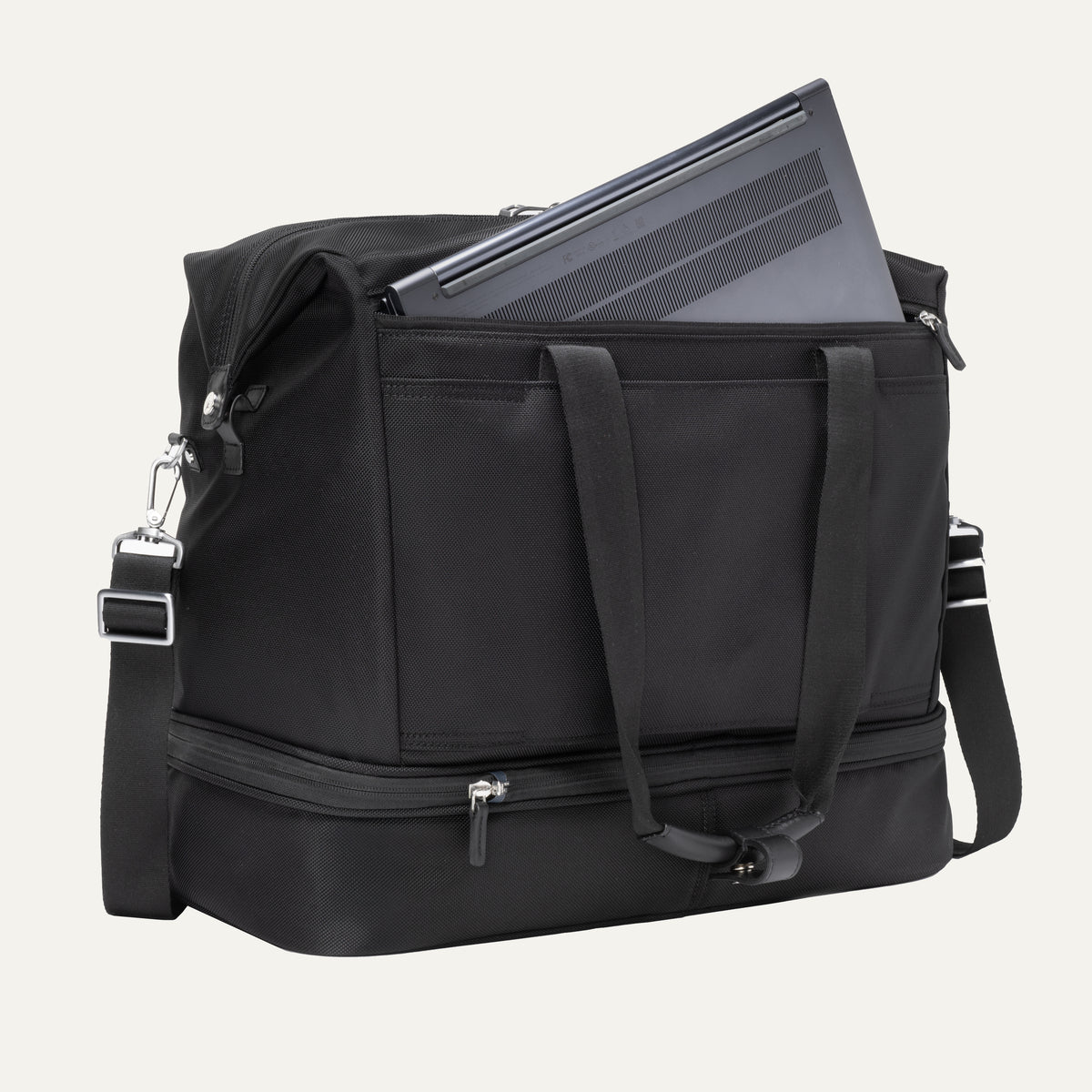 a black travelpro platinum elite drop-bottom weekender bag shown with a grey laptop being inserted into the internal padded electronics sleeve, highlighting the bag's organization and tech protection.