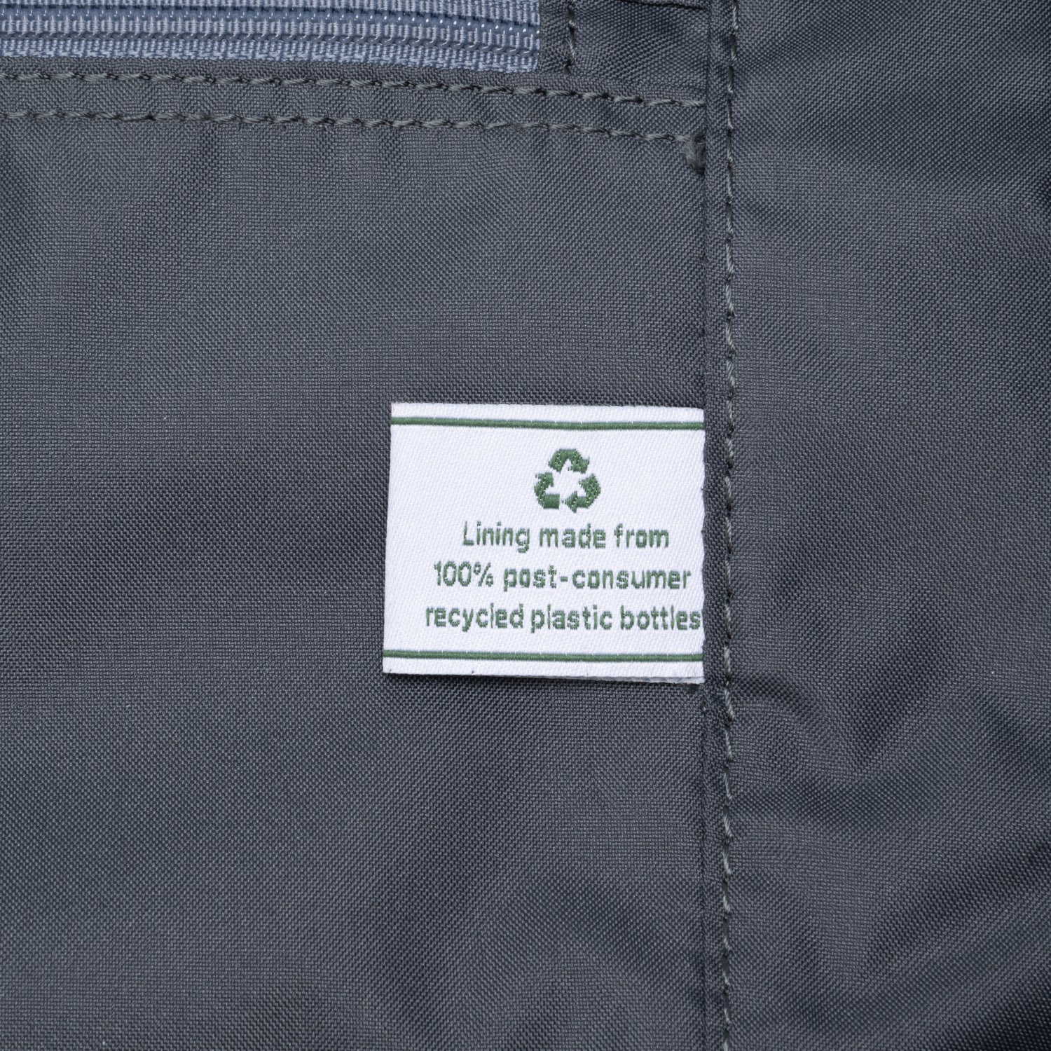 a close-up of the interior lining of the true navy travelpro platinum elite weekender bag, showing a white fabric label that reads "lining made from 100% post-consumer recycled plastic bottles" with a green recycling symbol.