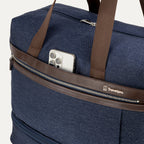 close-up of the front exterior of the true navy travelpro platinum elite weekender bag, showing a smartphone tucked into the quickslip pocket with premium chrome hardware and leather trim.