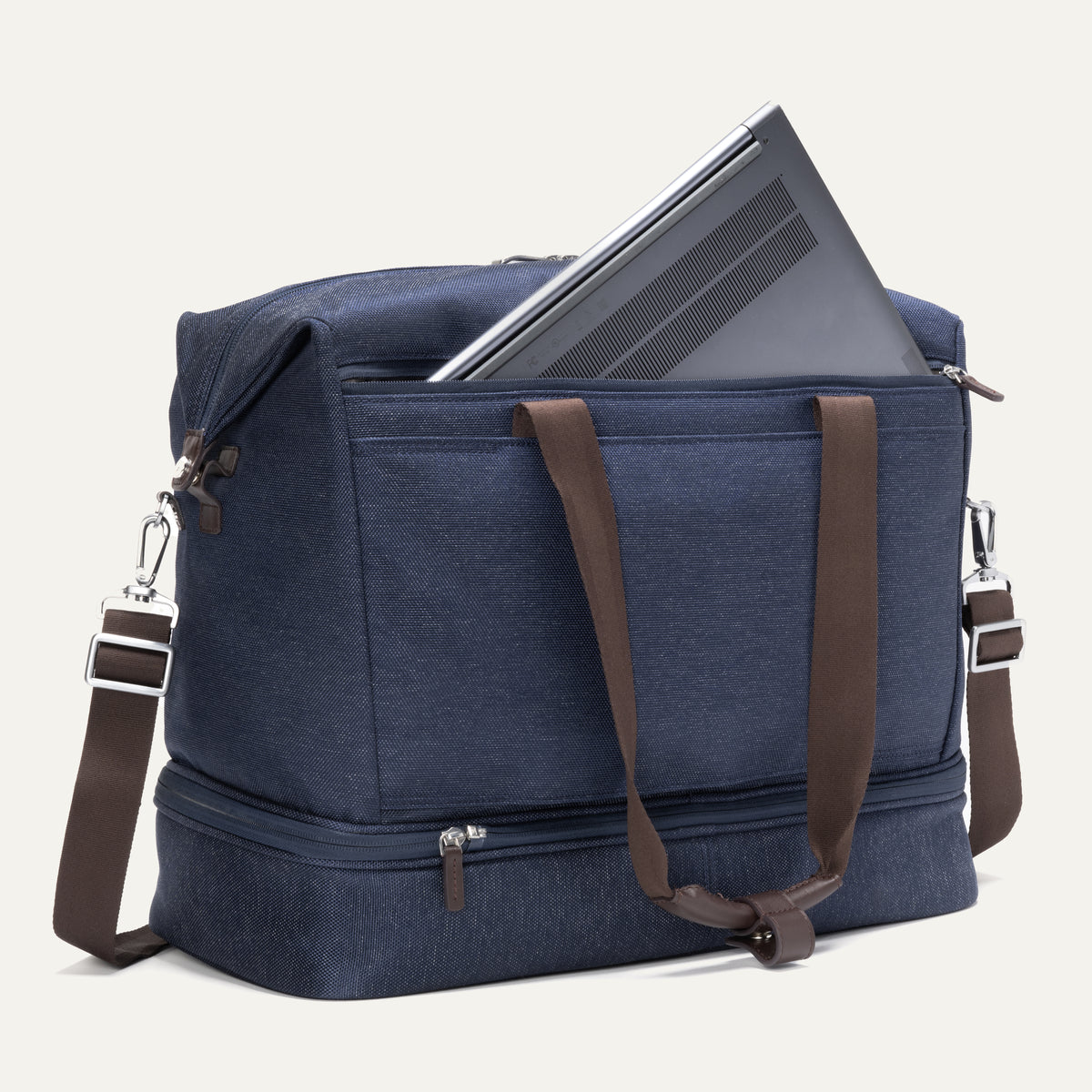 a true navy travelpro platinum elite drop-bottom weekender bag shown with a grey laptop being inserted into the internal padded electronics sleeve, highlighting the bag's organization and tech protection.
