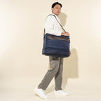 lifestyle shot of a male model walking while carrying the true navy travelpro platinum elite drop-bottom weekender bag using the adjustable shoulder strap, paired with casual white sneakers and tan trousers.