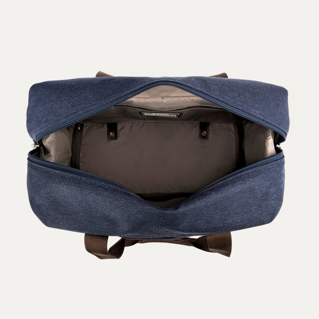 top-down view looking into the open drop-bottom compartment of the true navy travelpro platinum elite weekender bag, showing the interior organization, tan lining, and snap-button compression straps.