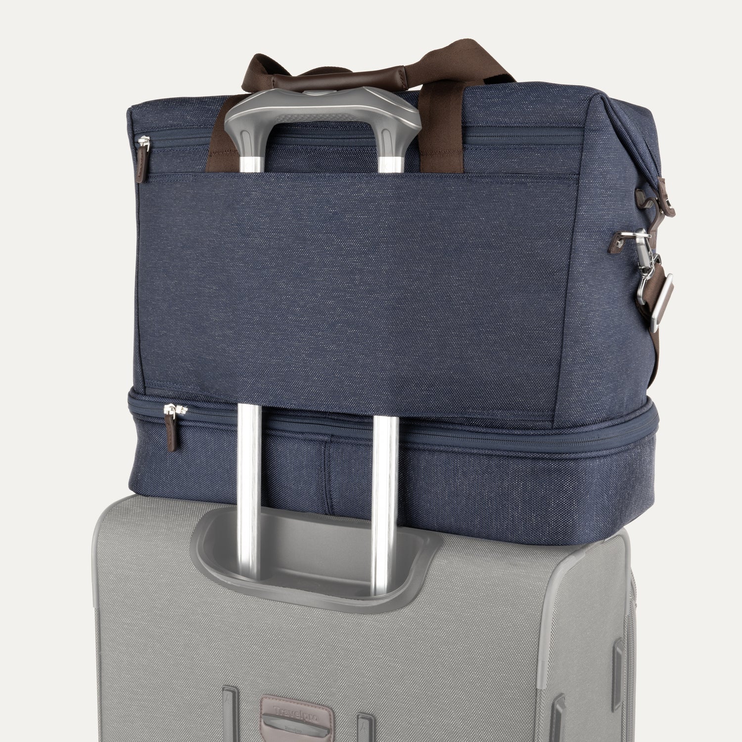 the true navy travelpro platinum elite weekender bag being stacked on a rolling suitcase, showing the integrated rear strap securely fitted over the luggage extension handle for hands-free transport.