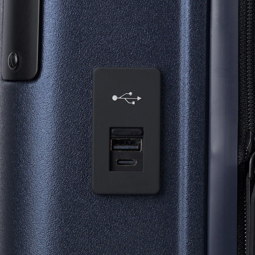 Macro detail view of the external USB-A and USB-C charging ports on the Travelpro Platinum Elite Carry-On Hardside Spinner in Aviator Navy, highlighting the integrated power connectivity for mobile devices.