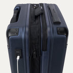 Close-up of the external charging ports on the Travelpro Platinum Elite Carry-On Hardside Spinner in Aviator Navy, showing a white cable plugged into the USB-A port and a power bank tucked into the dedicated battery sleeve within the expansion gusset.