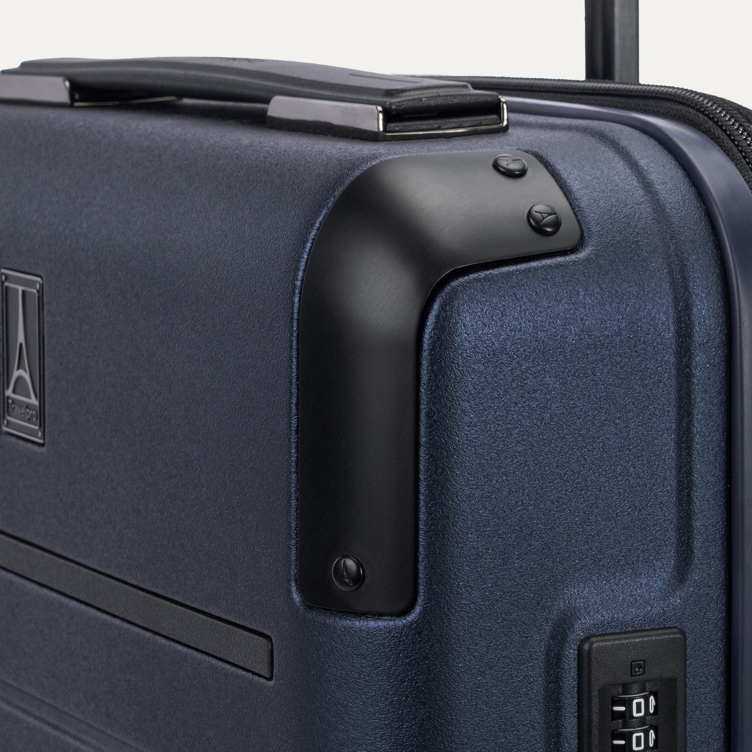 Close-up detail of the Travelpro Platinum Elite Carry-On Hardside Spinner in Aviator Navy, showing the protective corner armor and the integrated TSA-approved combination lock on the textured hardshell.