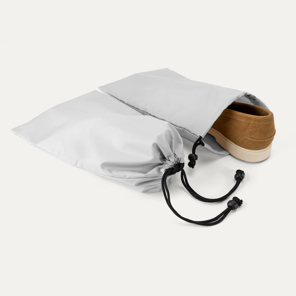 Close-up of the two removable grey drawstring shoe bags included with the Travelpro Platinum Elite Carry-On Hardside Spinner, showing a brown shoe partially inserted to demonstrate organizational use.