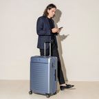 Lifestyle view of the Travelpro Platinum Elite Large Check-In Hardside Spinner in Dark Sky Blue, demonstrating the hands-free stability of the MagnaTrac self-aligning spinner wheels that track straight during transit.