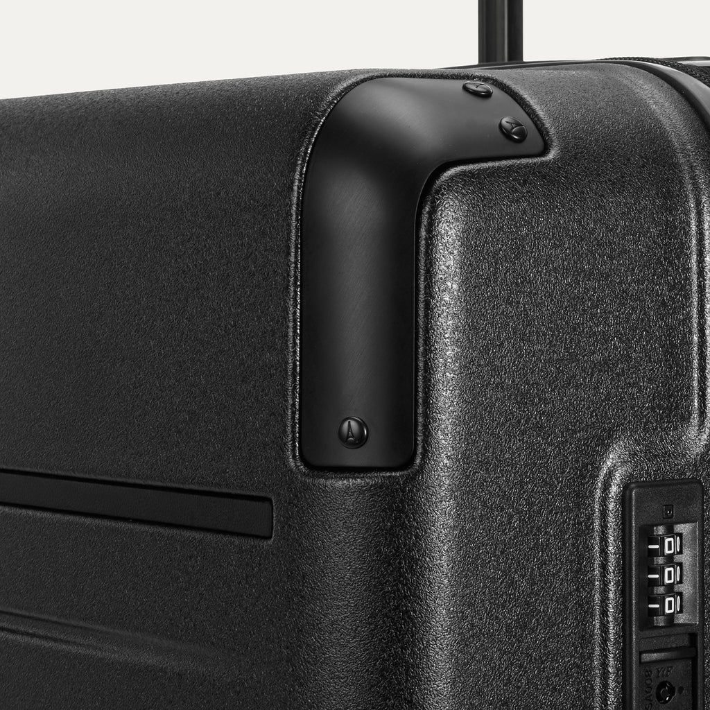 Close-up detail of the Travelpro Platinum Elite Large Check-In Hardside Spinner in Jet Black, showing the integrated TSA-approved combination lock and protective aluminum corner armor.