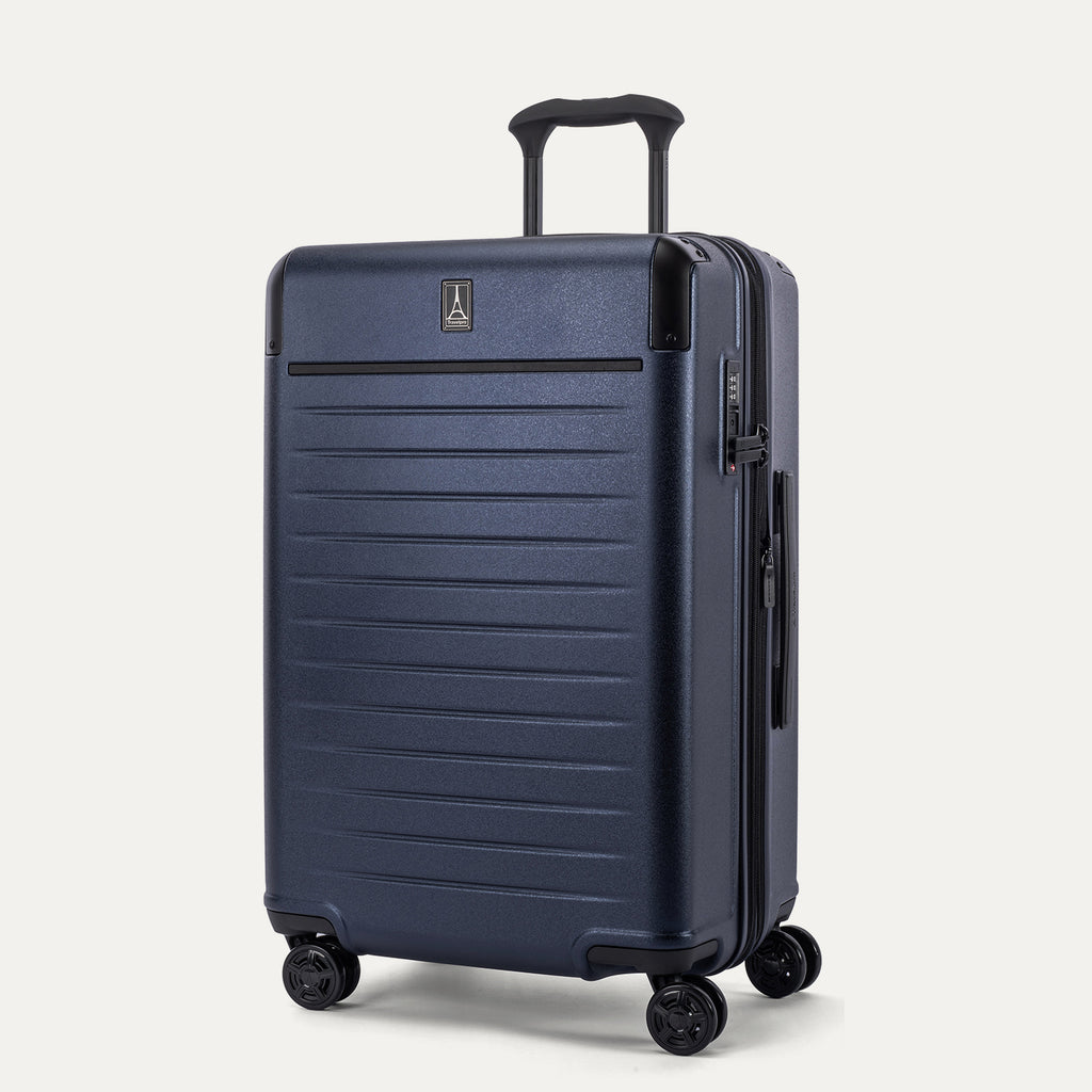 Front 3/4 view of the Travelpro Platinum Elite Medium Check-In Hardside Spinner in Aviator Navy, featuring a scuff-resistant polycarbonate shell, aluminum corner armor, and 360-degree spinner wheels.
