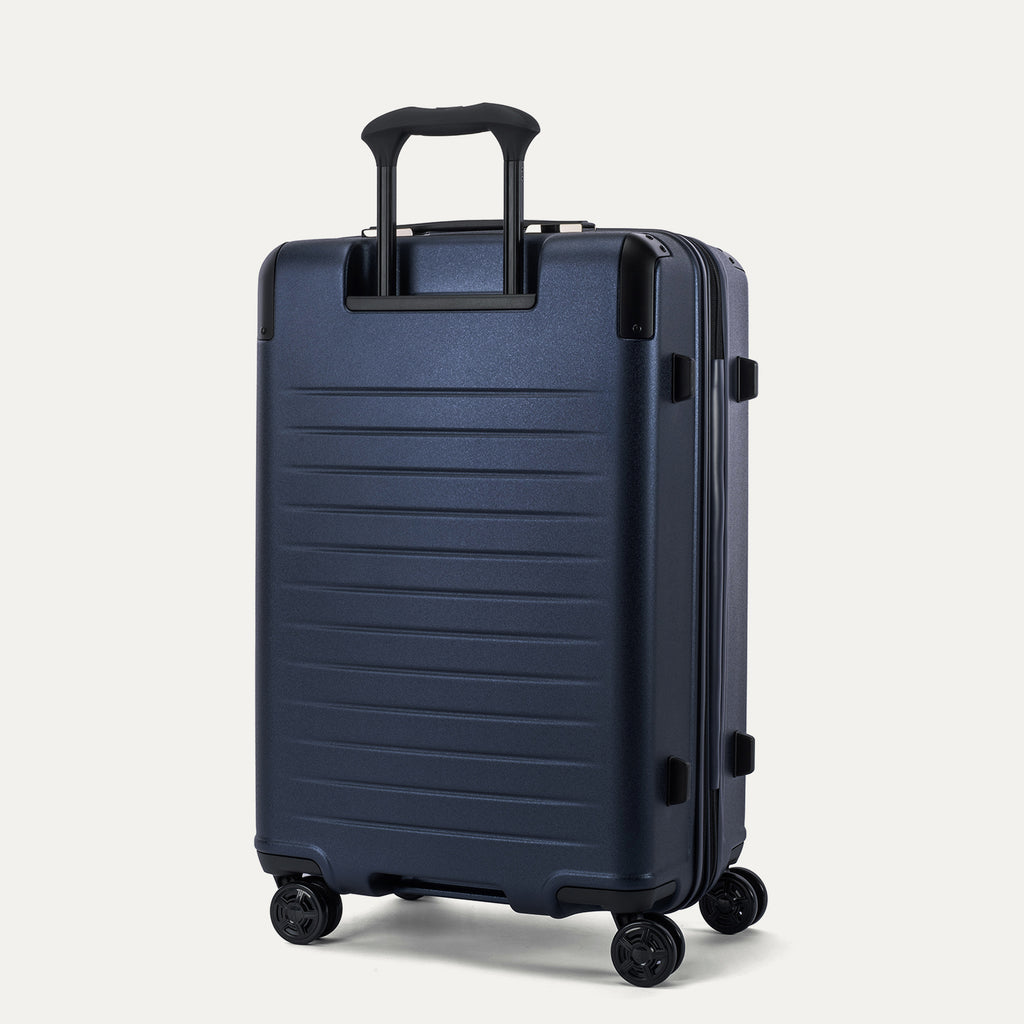 Rear 3/4 view of the Travelpro Platinum Elite Medium Check-In Hardside Spinner in Aviator Navy, featuring the sturdy PowerScope Lite handle and high-performance, self-aligning spinner wheels.