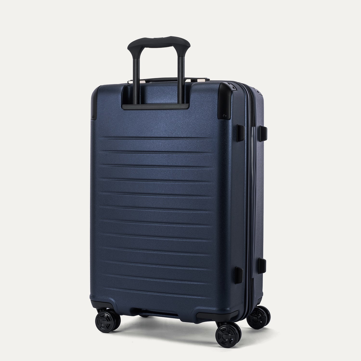 Rear 3/4 view of the Travelpro Platinum Elite Medium Check-In Hardside Spinner in Aviator Navy, featuring the sturdy PowerScope Lite handle and high-performance, self-aligning spinner wheels.