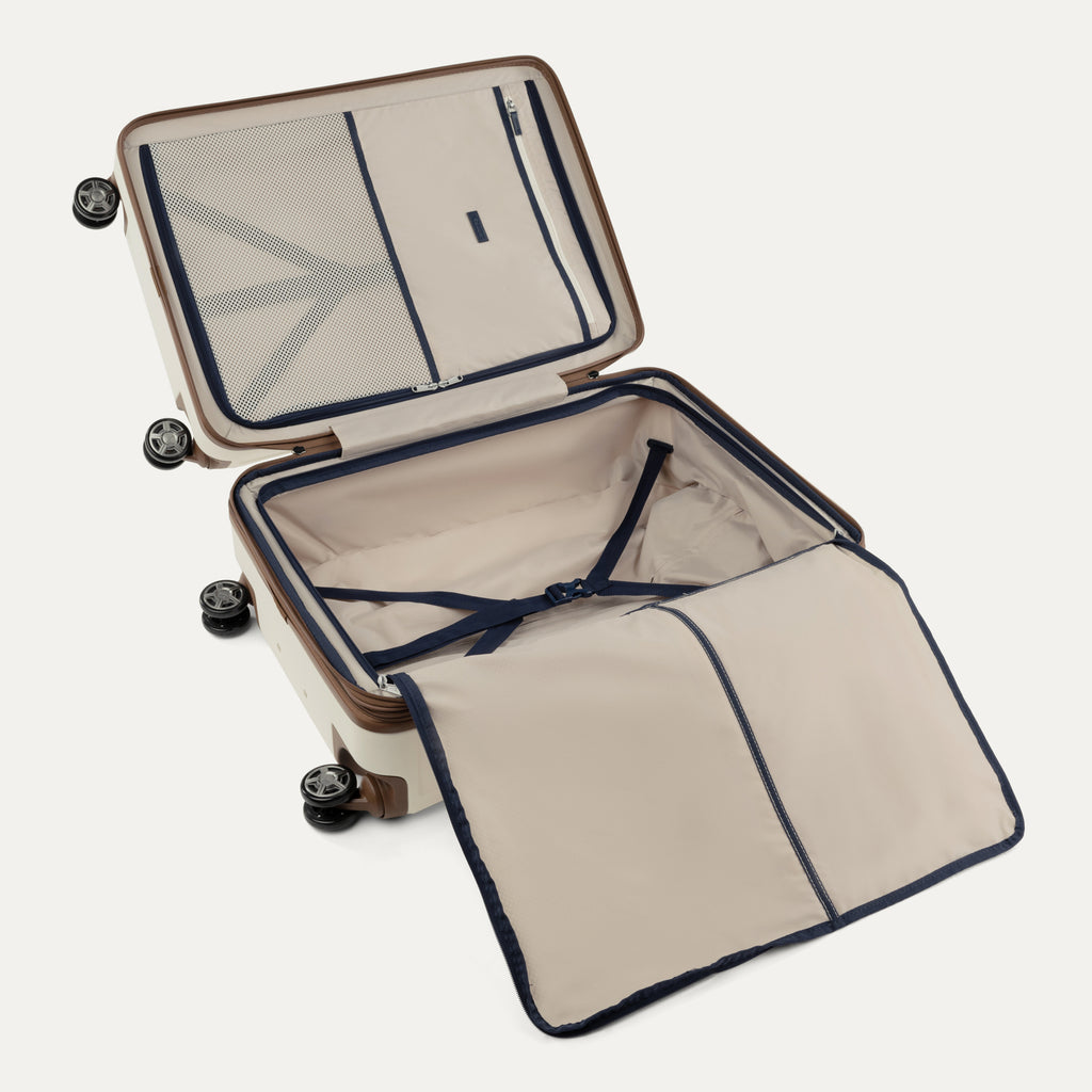 "Interior view of the Travelpro Platinum Elite Medium Check-In Hardside Spinner in Cream White, showcasing the dual zippered divider panels, adjustable hold-down straps, and premium interior lining with brown leather accents."