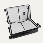 Interior packing view of the Travelpro Platinum Elite Medium Check-In Hardside Spinner in Jet Black, featuring dual zippered divider panels, multiple accessory pockets, and a water-resistant compartment.