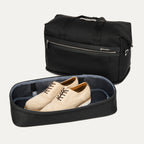 a view of the shadow black travelpro platinum elite weekender bag with the drop-bottom compartment zipped open, showing a pair of tan brogue shoes stored separately from the main packing area.