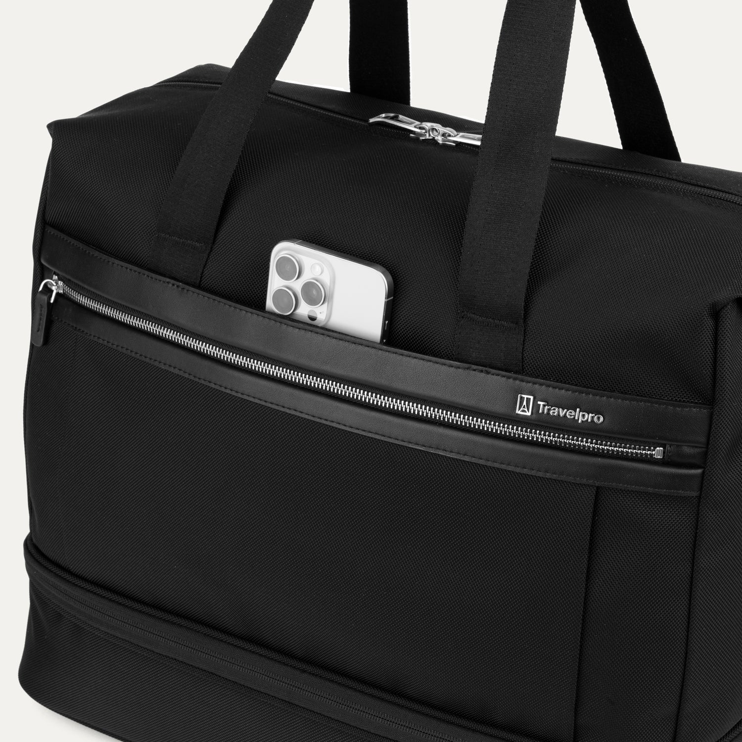 close-up of the front exterior of the shadow black travelpro platinum elite weekender bag, showing a smartphone tucked into the quick-access zippered pocket with premium chrome hardware and leather trim.