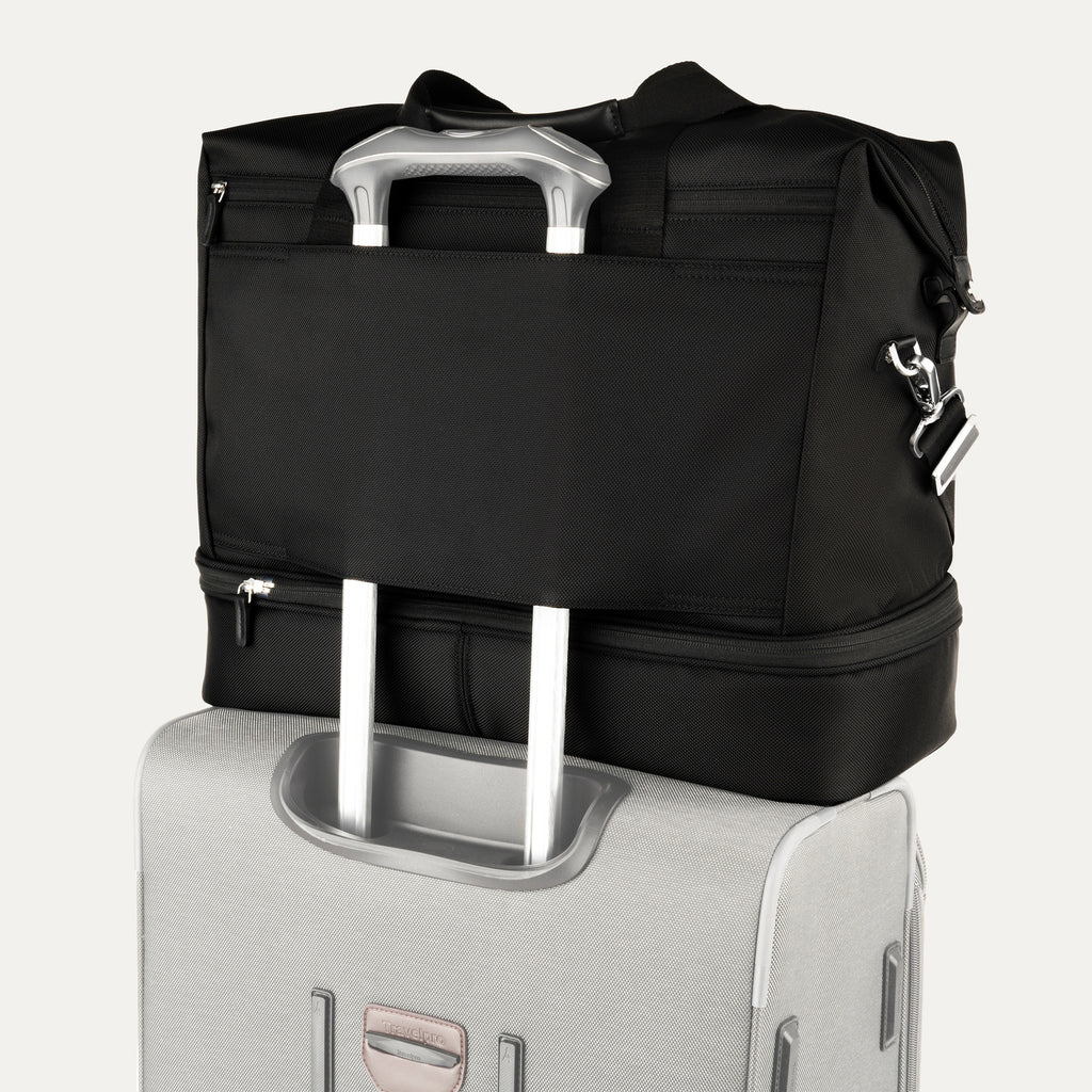 rear view of the shadow black travelpro platinum elite drop-bottom weekender bag, showing the integrated trolley sleeve securely stacked over the telescoping handle of a hardside suitcase for easy mobility.
