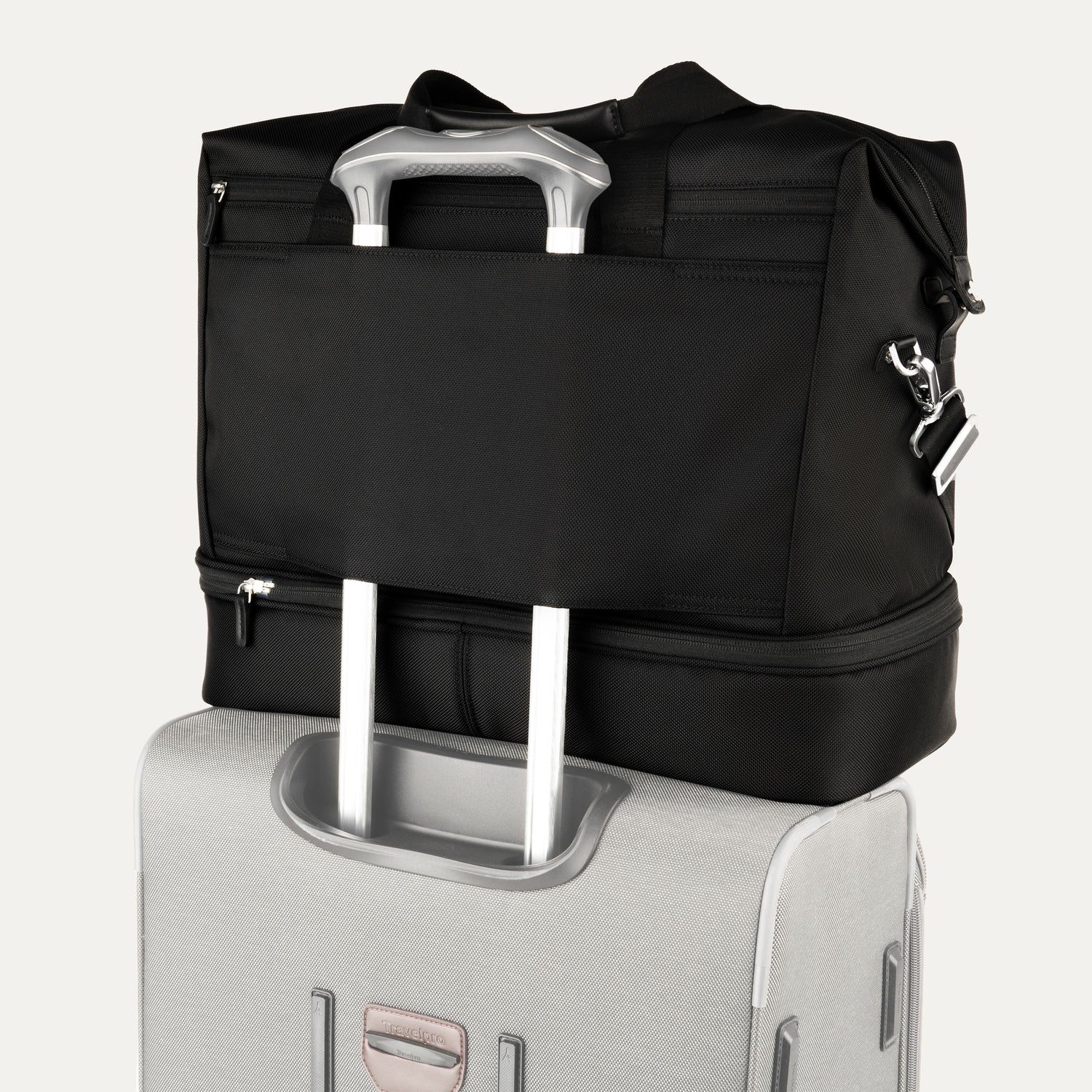 rear view of the shadow black travelpro platinum elite drop-bottom weekender bag, showing the integrated trolley sleeve securely stacked over the telescoping handle of a hardside suitcase for easy mobility.