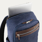close-up view of the true navy travelpro platinum® elite slim laptop backpack 16l, showing a silver laptop being inserted into the padded rear electronics compartment with dark brown leather trim.