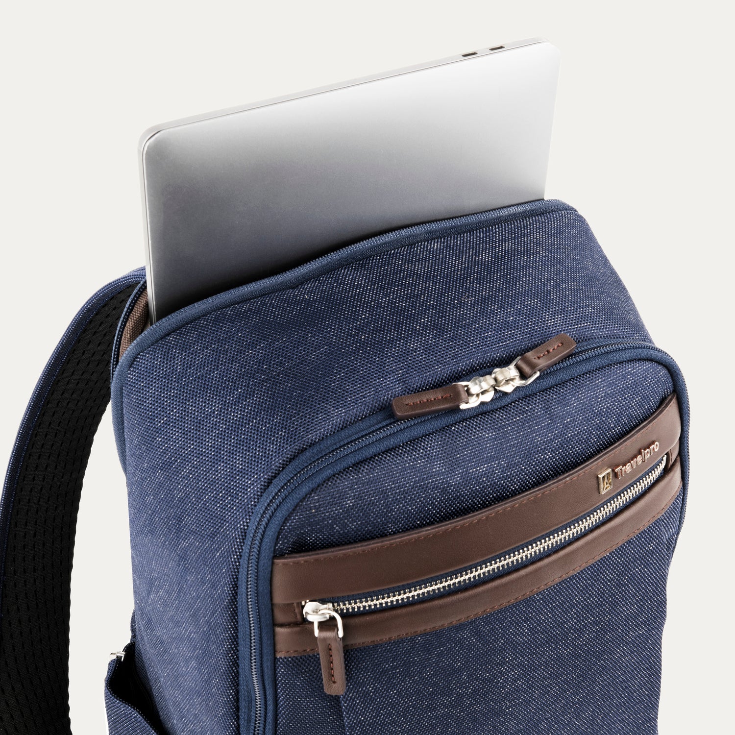 close-up view of the true navy travelpro platinum® elite slim laptop backpack 16l, showing a silver laptop being inserted into the padded rear electronics compartment with dark brown leather trim.