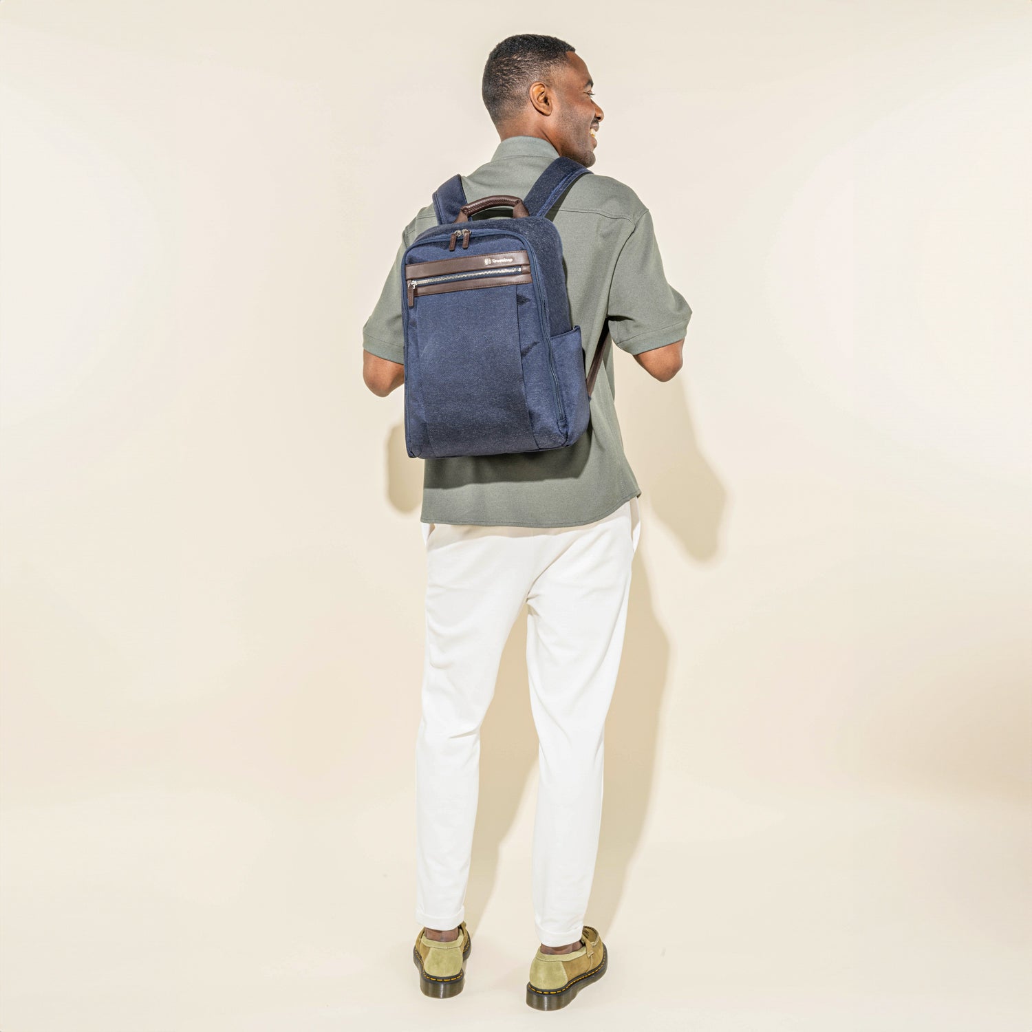rear lifestyle view of a male model wearing the true navy travelpro platinum® elite slim laptop backpack 16l, showing the bag's slim profile against an olive green shirt and white trousers.
