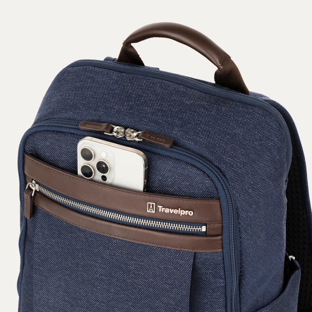close-up view of the true navy travelpro platinum® elite slim laptop backpack 16l, showing a white smartphone being tucked into the magnetic quickslip front pocket with dark brown leather trim.