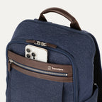 close-up view of the true navy travelpro platinum® elite slim laptop backpack 16l, showing a white smartphone being tucked into the magnetic quickslip front pocket with dark brown leather trim.