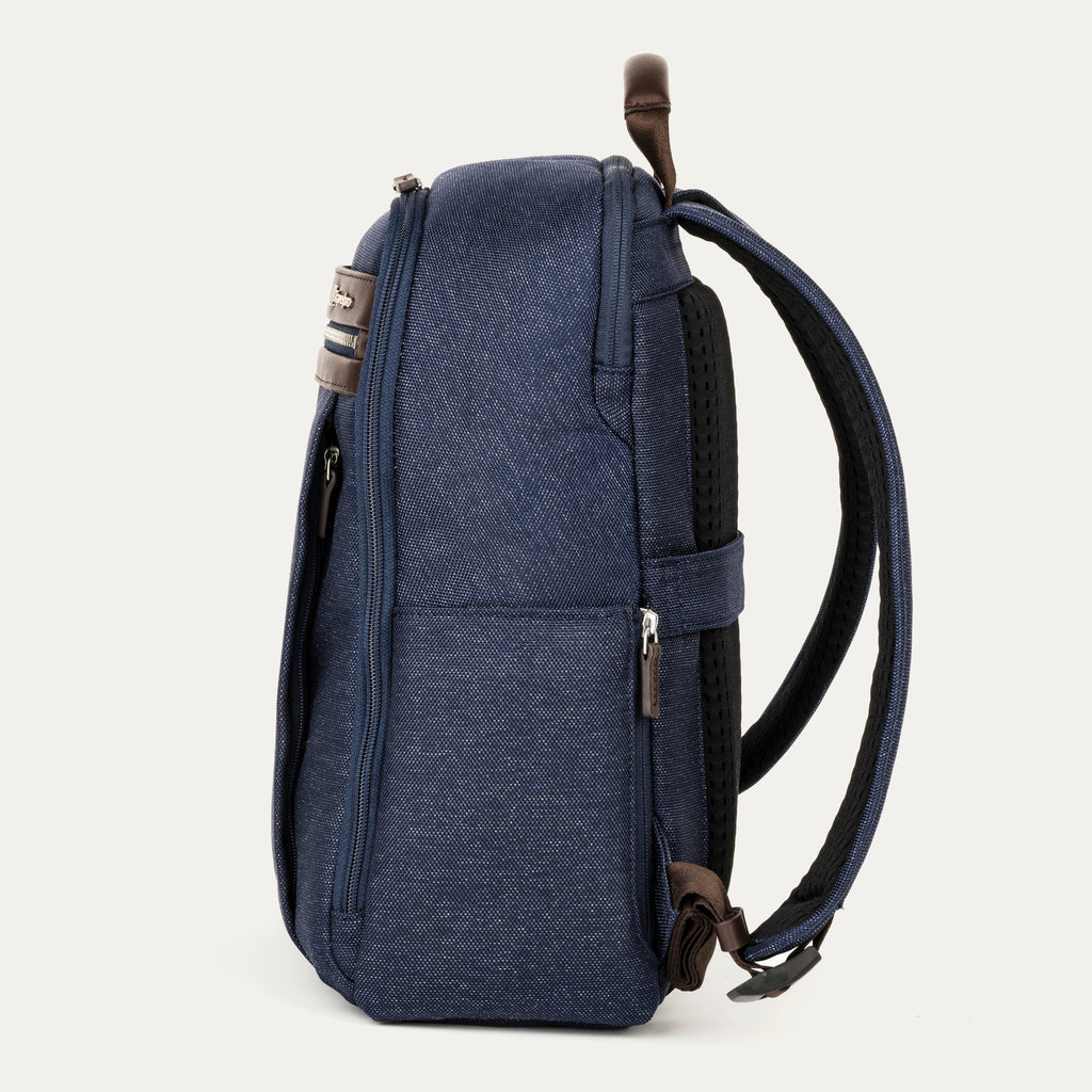 side profile view of the true navy travelpro platinum® elite slim laptop backpack 16l, showing its thin design, textured navy fabric, and dark brown leather accents on the top handle and zipper pulls.