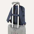 rear view of the true navy travelpro platinum® elite slim laptop backpack 16l stacked on a grey rolling suitcase, showing the integrated trolley strap with dark brown leather accents secured over the extension handle.