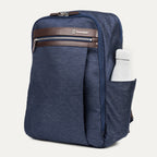 side profile of the true navy travelpro platinum® elite slim laptop backpack 16l, showing a white reusable water bottle tucked into the integrated side pocket with dark brown leather trim.