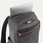 close-up view of the vintage grey travelpro platinum® elite slim laptop backpack 16l, showing a silver laptop being inserted into the padded rear electronics compartment with dark brown leather trim.