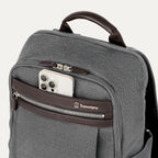 close-up view of the vintage grey travelpro platinum® elite slim laptop backpack 16l, showing a white smartphone being tucked into the magnetic quickslip front pocket with dark brown leather trim.
