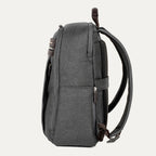 side profile view of the vintage grey travelpro platinum® elite slim laptop backpack 16l, highlighting its thin design, textured grey fabric, and dark brown leather accents on the top handle and zipper pulls.