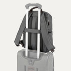 rear view of the vintage grey travelpro platinum® elite slim laptop backpack 16l stacked on a grey rolling suitcase, showing the integrated trolley strap with dark brown leather accents secured over the extension handle.