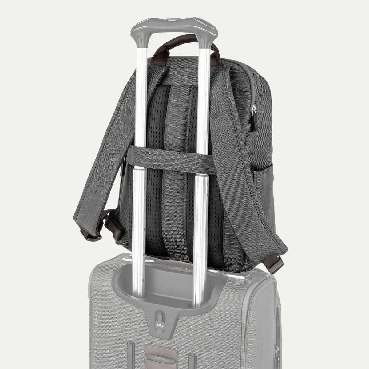 rear view of the vintage grey travelpro platinum® elite slim laptop backpack 16l stacked on a grey rolling suitcase, showing the integrated trolley strap with dark brown leather accents secured over the extension handle.