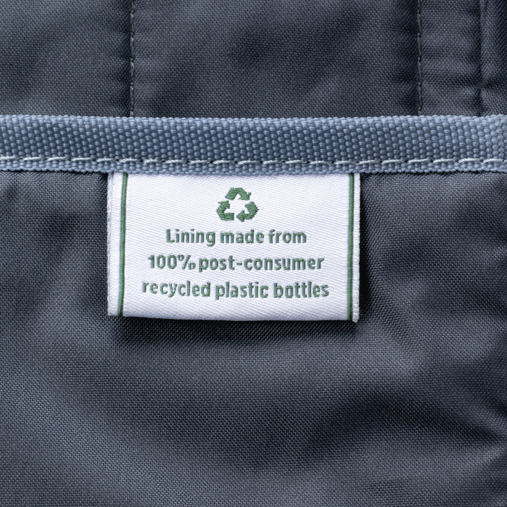 close-up of the grey interior lining of the black travelpro platinum elite underseat tote, showing a white fabric label with a green recycling symbol that reads "lining made from 100% post-consumer recycled plastic bottles."