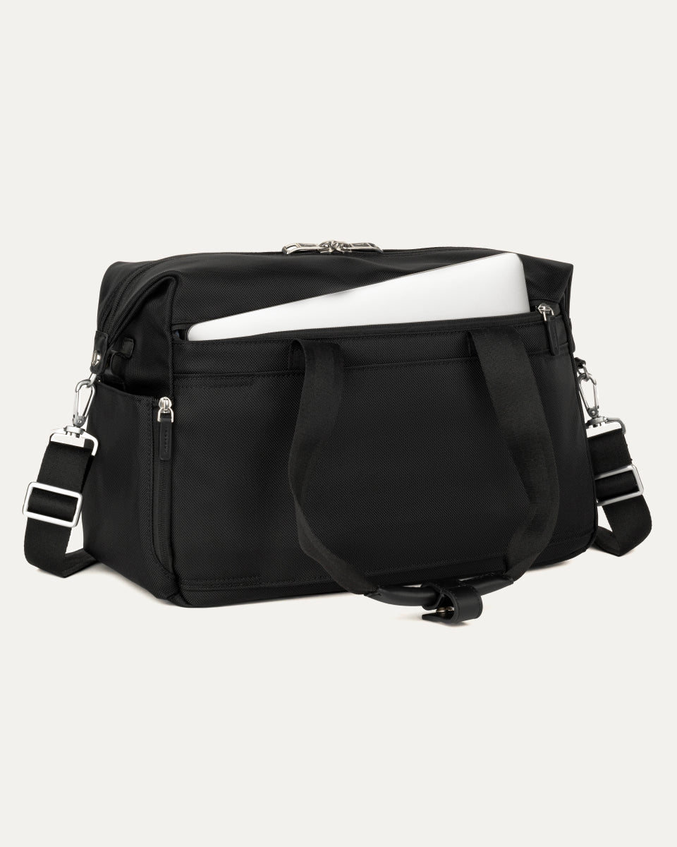 a black travelpro platinum elite underseat tote shown with a white laptop being inserted into the internal padded electronics sleeve, highlighting the bag's organization and protection for tech devices.