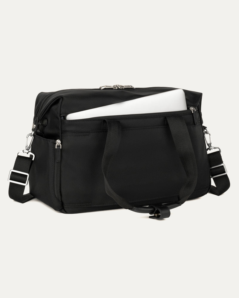 a black travelpro platinum elite underseat tote shown with a white laptop being inserted into the internal padded electronics sleeve, highlighting the bag's organization and protection for tech devices.