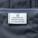 close-up of the interior lining of the true navy travelpro platinum elite underseat tote, showing a white fabric label with a green recycling symbol that reads "lining made from 100% post-consumer recycled plastic bottles."