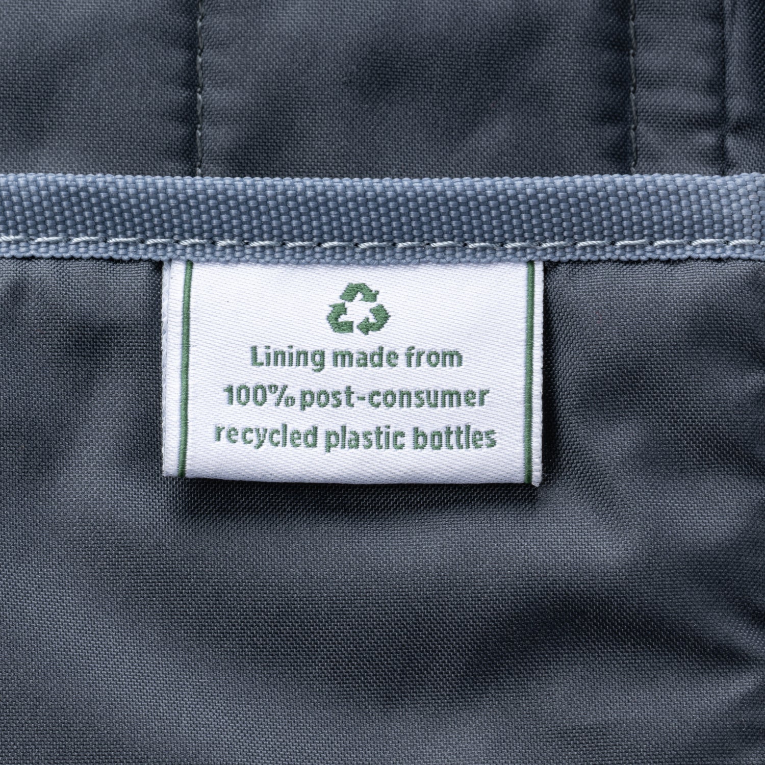 close-up of the interior lining of the true navy travelpro platinum elite underseat tote, showing a white fabric label with a green recycling symbol that reads "lining made from 100% post-consumer recycled plastic bottles."
