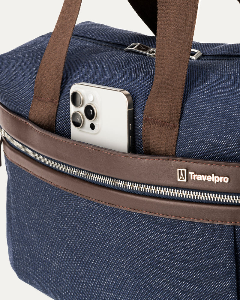 close-up of the front exterior of the true navy travelpro platinum elite underseat tote, showing a smartphone tucked into the quickslip pocket with brown leather trim and the travelpro logo.