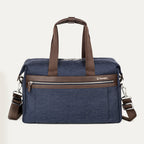 front view of the true navy travelpro platinum elite underseat tote featuring a textured blue fabric, brown leather trim and handles, chrome hardware, and a removable shoulder strap.