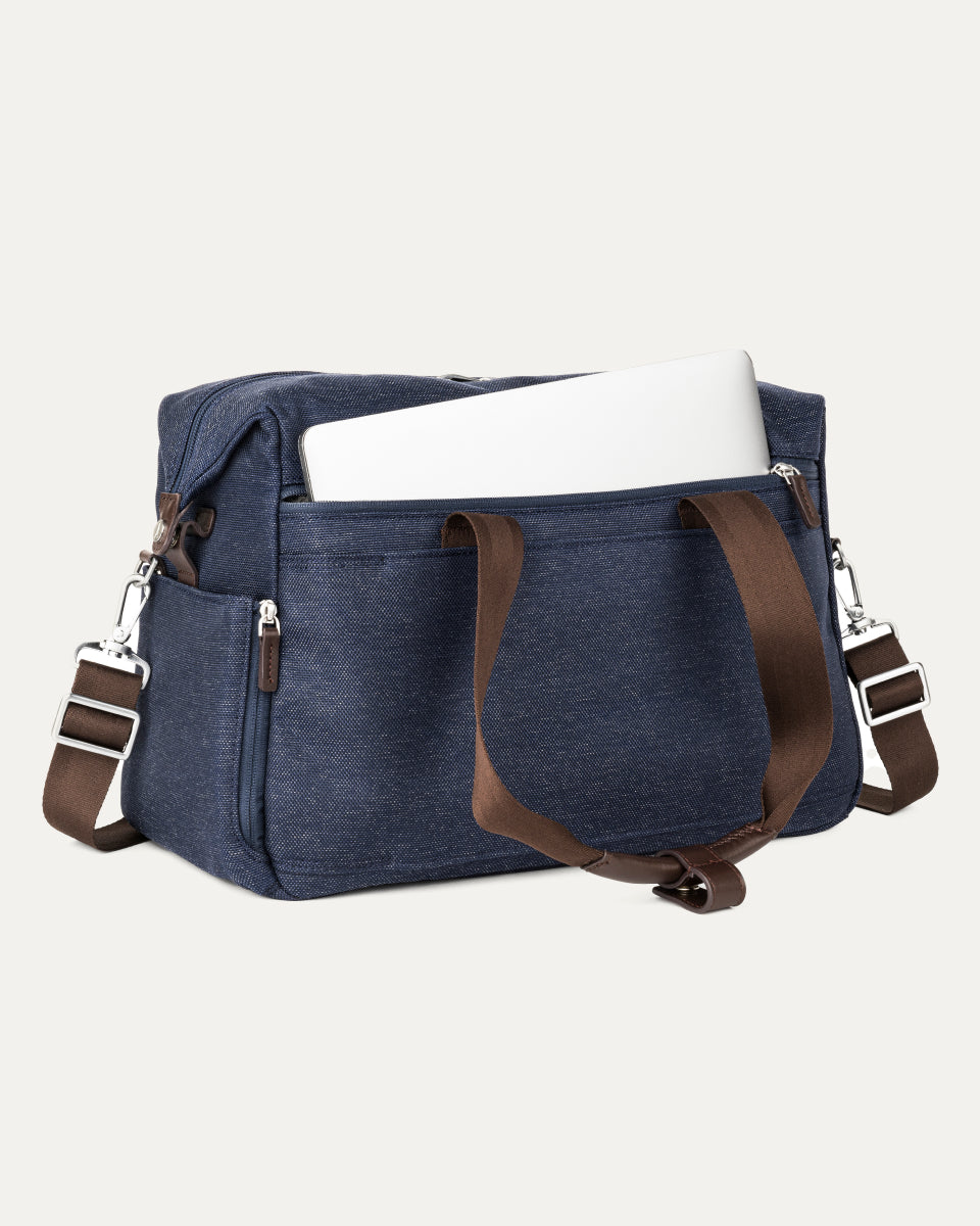 a true navy travelpro platinum elite underseat tote shown with a white laptop being inserted into the internal padded electronics sleeve, highlighting the bag's organization and protection for tech devices.