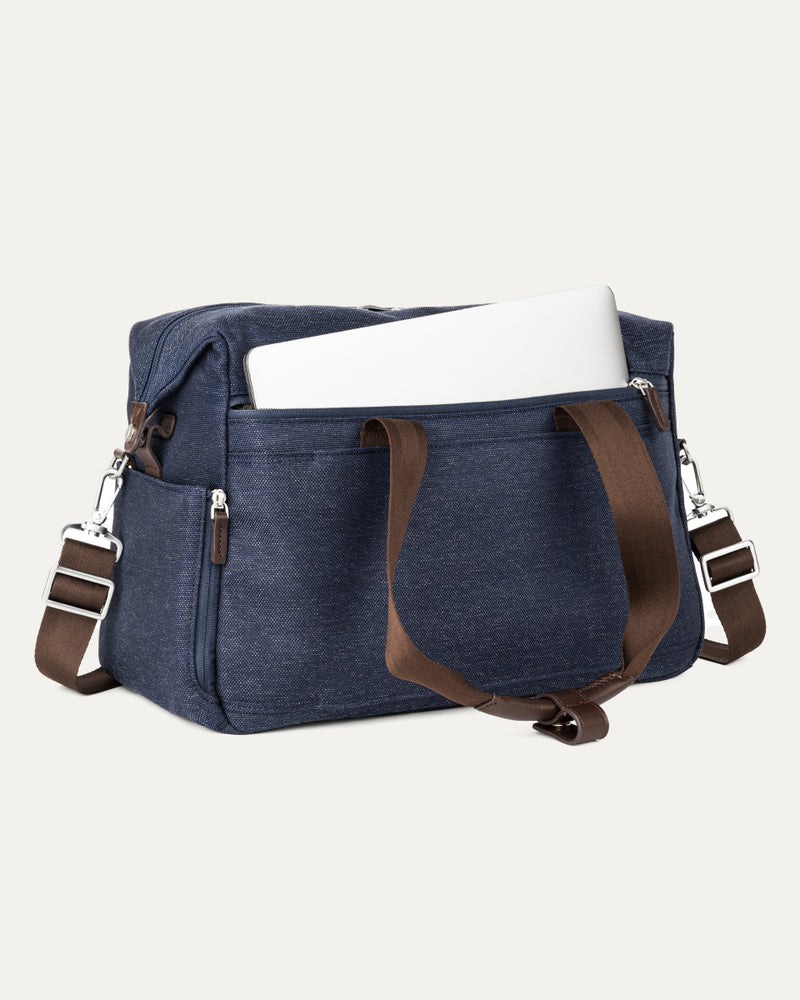 a true navy travelpro platinum elite underseat tote shown with a white laptop being inserted into the internal padded electronics sleeve, highlighting the bag's organization and protection for tech devices.