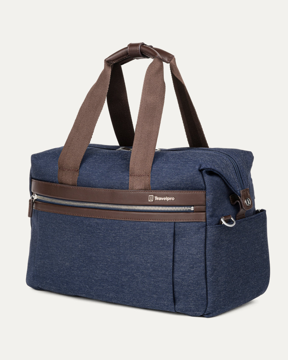 a three-quarter perspective view of the true navy travelpro platinum elite underseat tote, highlighting the textured blue fabric, brown leather trim, front zippered pocket, and side accessory pocket.