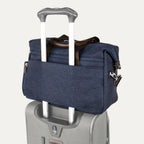 a true navy travelpro platinum elite underseat tote stacked on top of a silver rolling suitcase, with its integrated rear trolley strap securely slid over the luggage extension handle for easy transport.