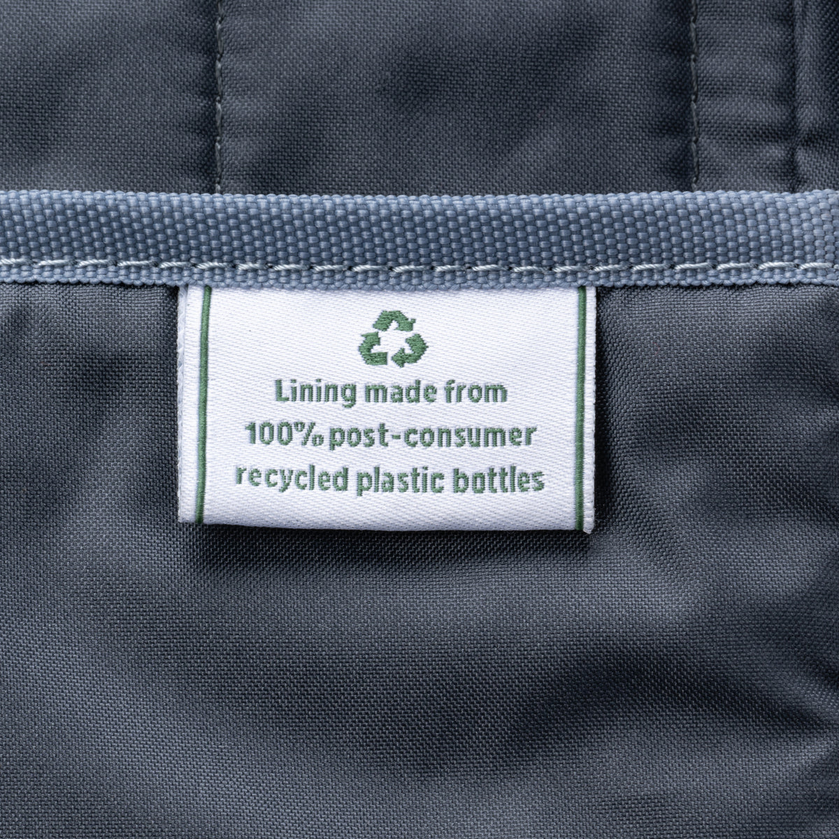 close-up of the tan interior lining of the vintage grey travelpro platinum elite underseat tote, showing a white fabric label with a green recycling symbol that reads "lining made from 100% post-consumer recycled plastic bottles."