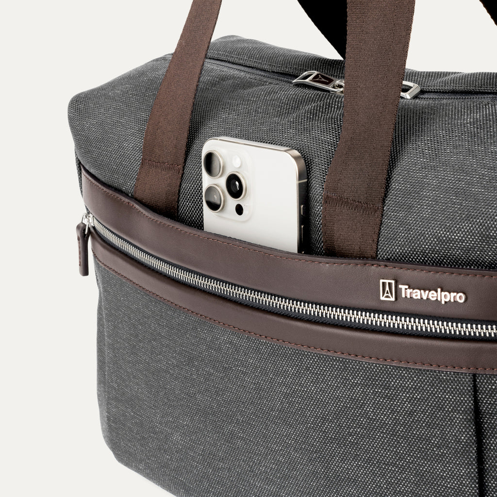 close-up of the front exterior of the vintage grey travelpro platinum elite underseat tote, showing a smartphone tucked into the quickslip pocket with brown leather trim and the travelpro logo.